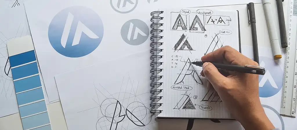 A végleges logó többféle színváltozatban kinyomtatva a tervező asztalon, mellette a kiválasztott színskála.