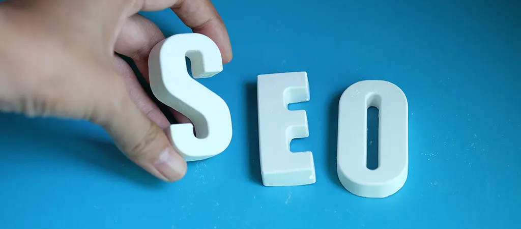 Egy kéz a SEO szó betűit igazítja egymáshoz kék háttéren, utalva a domain név SEO szempontú jelentőségére.